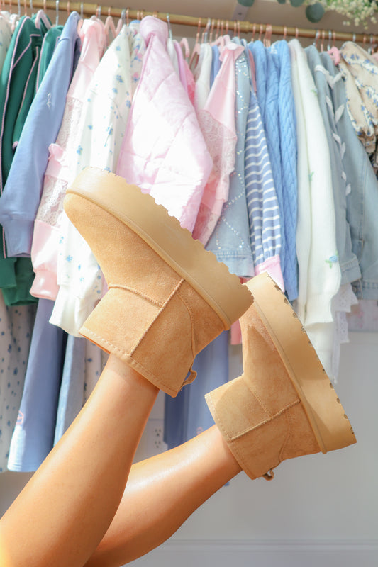 Tan suede platform booties worn with pastel clothes hanging in background