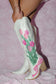 Hand-painted white cowgirl boots with pink tulips and pink bow styled on pink lace background